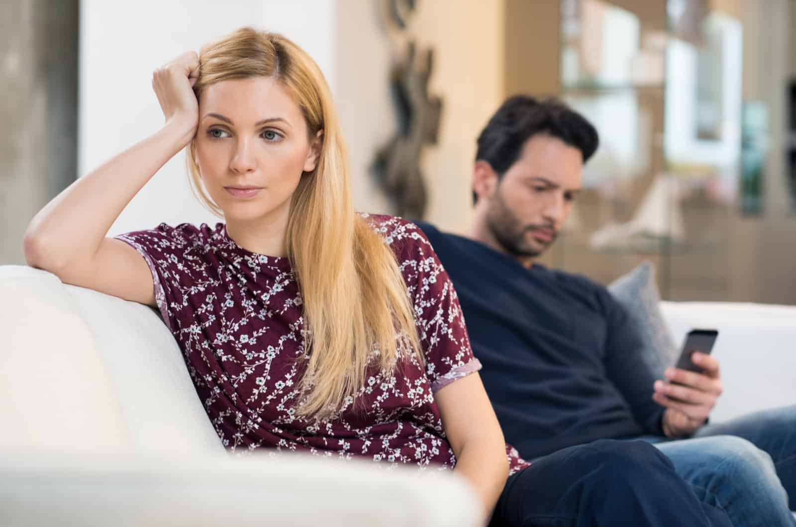 surullinen nainen istuu sohvalla miehen kanssa taustalla
