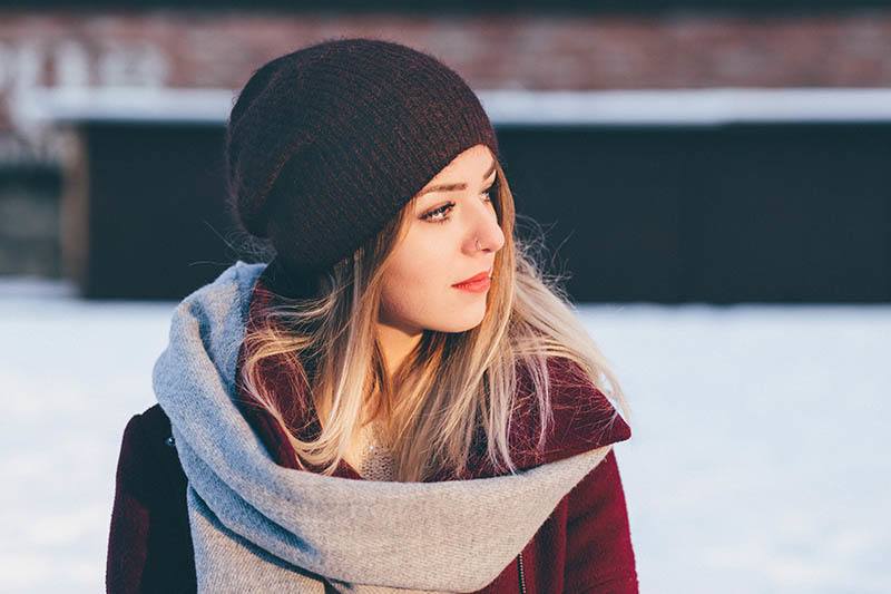 Eine traurige Frau mit einer schwarzen M&uuml;tze steht im Schnee und schaut weg