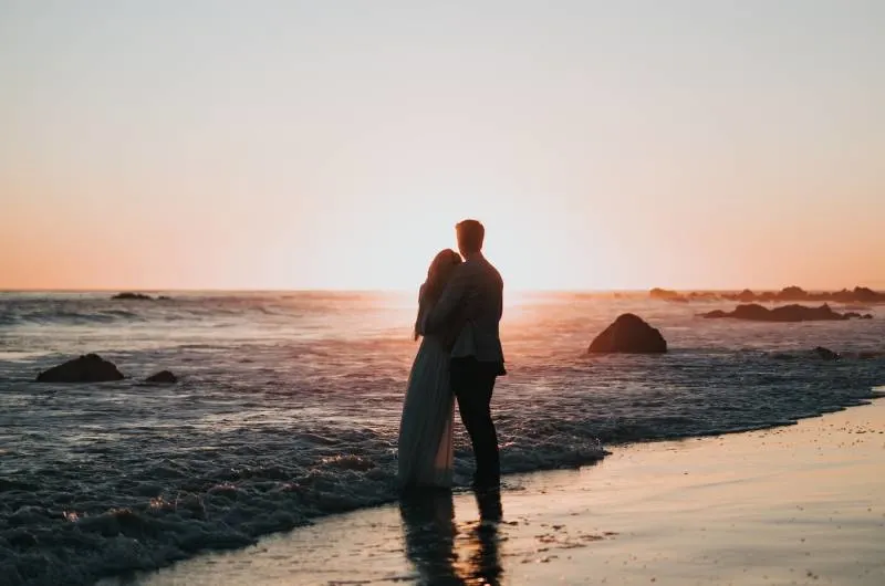 Schattenbildfoto des Paares, das am Strand steht und Sonnenuntergang beobachtet Schattenbildfoto des Paares, das am Strand steht und Sonnenuntergang beobachtet